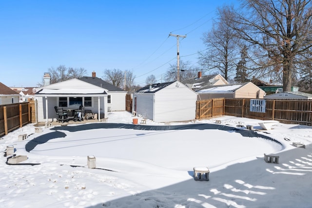 yard layered in snow featuring an outbuilding, a storage shed, and a fenced backyard