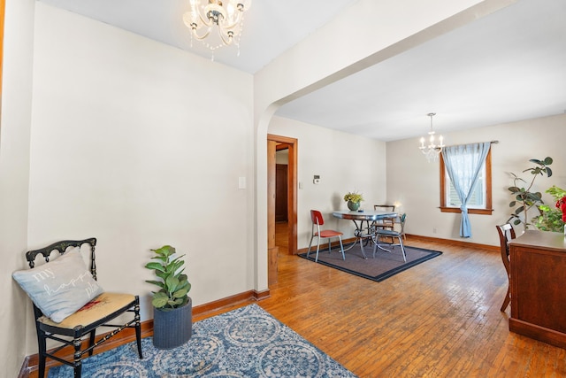 dining room with arched walkways, a notable chandelier, baseboards, and wood finished floors