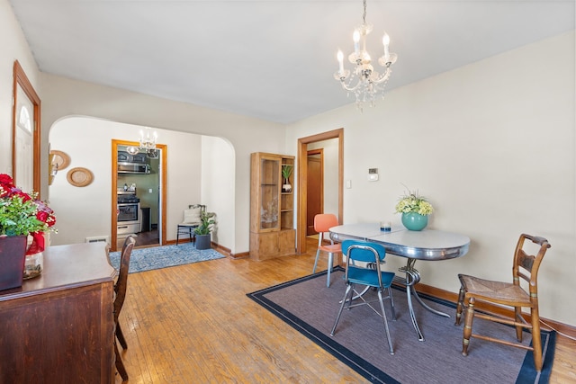 dining space featuring arched walkways, baseboards, light wood-style flooring, and a notable chandelier