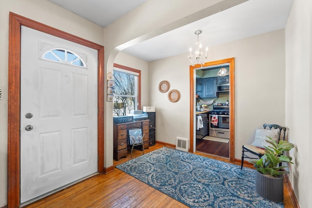 entrance foyer with arched walkways, wood finished floors, visible vents, baseboards, and an inviting chandelier