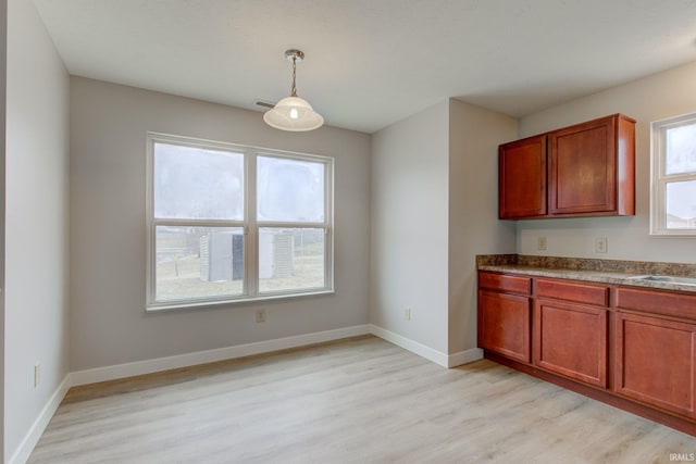 kitchen with hanging light fixtures, light wood-type flooring, baseboards, and a wealth of natural light