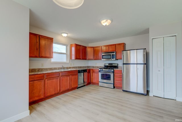 kitchen featuring light wood finished floors, stainless steel appliances, light countertops, brown cabinetry, and a sink