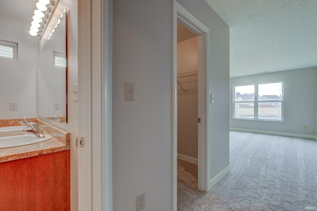 bathroom featuring a textured ceiling, a sink, baseboards, double vanity, and a walk in closet