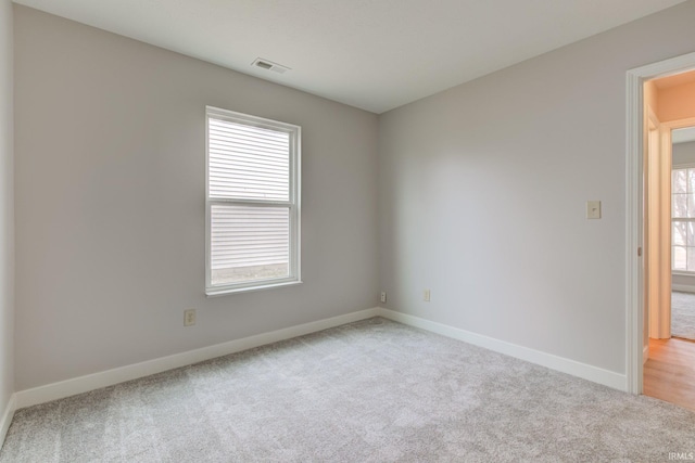 empty room featuring light carpet, visible vents, and baseboards