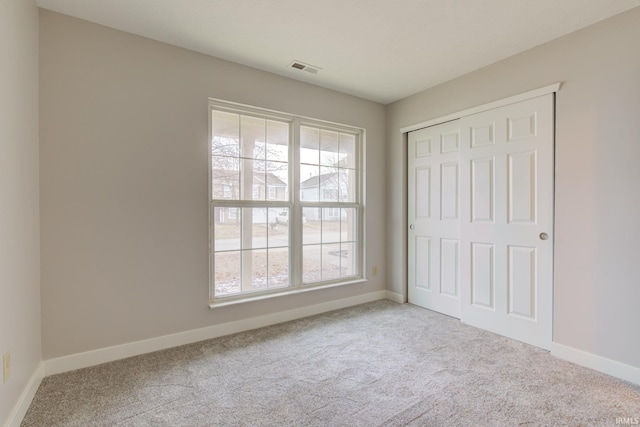 unfurnished bedroom with light carpet, a closet, visible vents, and baseboards