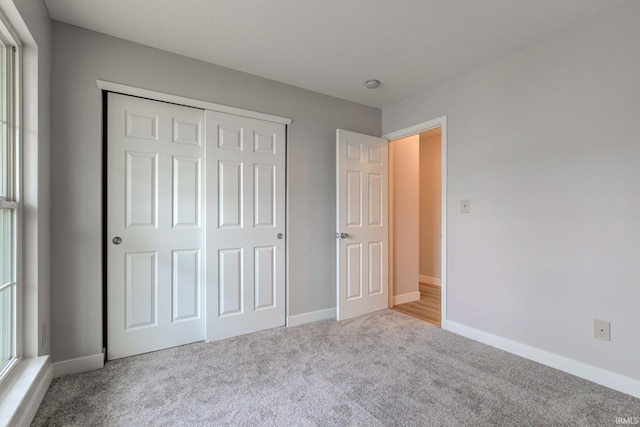 unfurnished bedroom featuring a closet, light colored carpet, and baseboards