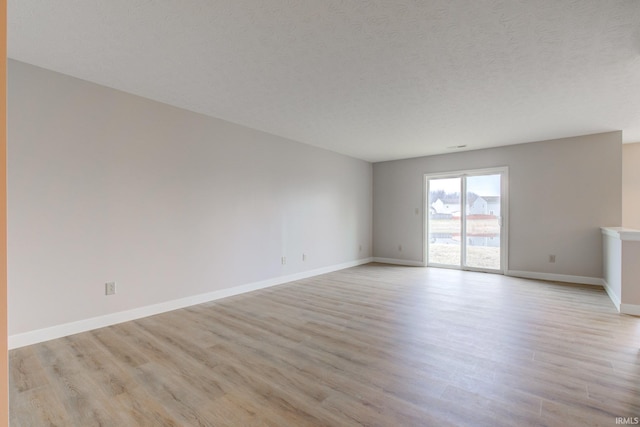 spare room featuring light wood-type flooring, a textured ceiling, and baseboards