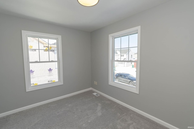 carpeted empty room featuring visible vents, a wealth of natural light, and baseboards