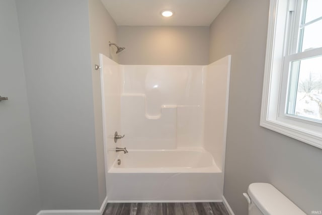 bathroom featuring baseboards, bathing tub / shower combination, toilet, and wood finished floors