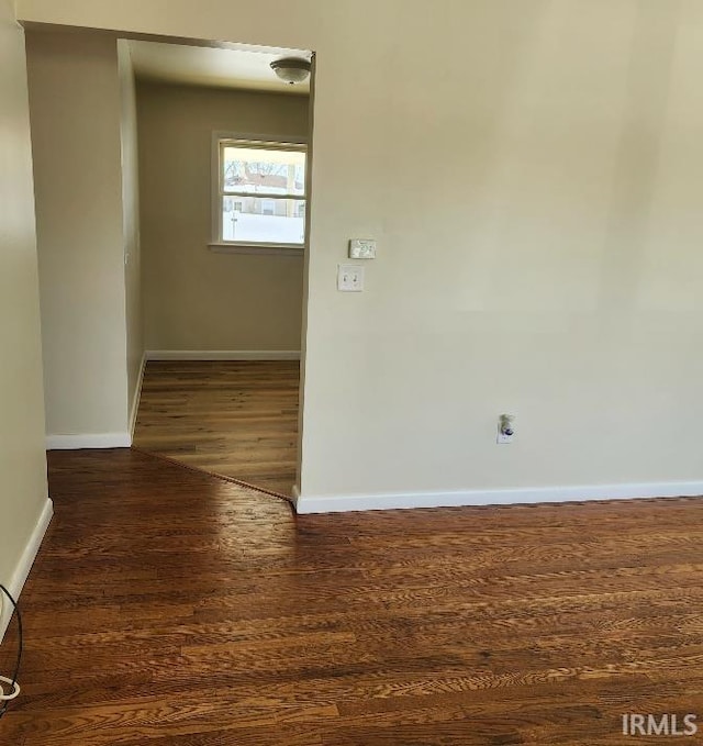 spare room featuring dark wood-style flooring and baseboards