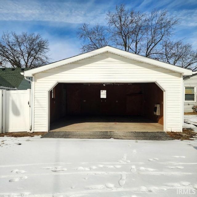 snow covered garage with a detached garage and fence