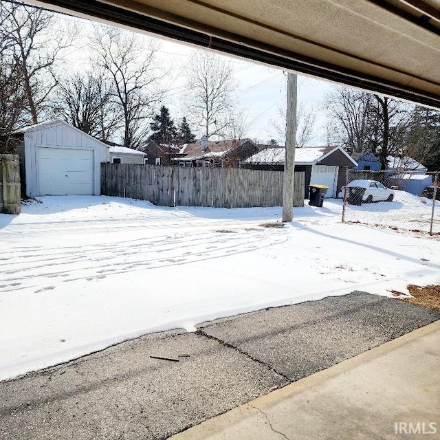 yard covered in snow featuring a garage, an outbuilding, and fence