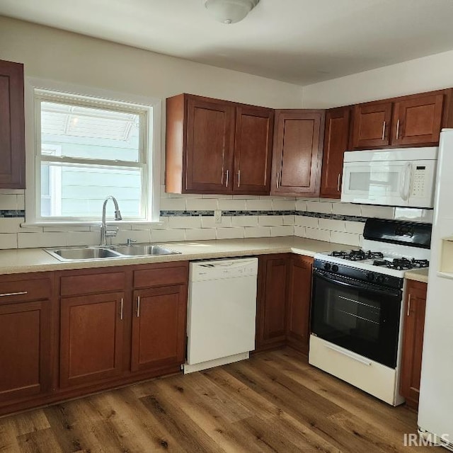 kitchen featuring dark wood finished floors, light countertops, decorative backsplash, a sink, and white appliances