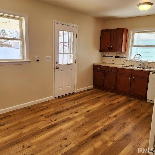 kitchen with light wood finished floors, light countertops, a sink, dishwasher, and baseboards