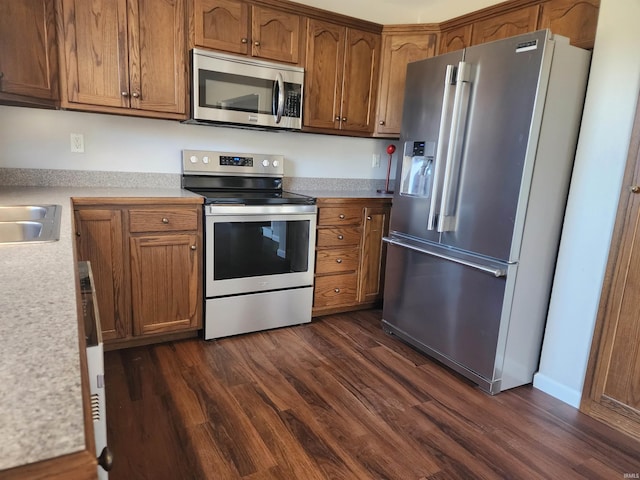 kitchen with appliances with stainless steel finishes, brown cabinets, light countertops, and dark wood finished floors