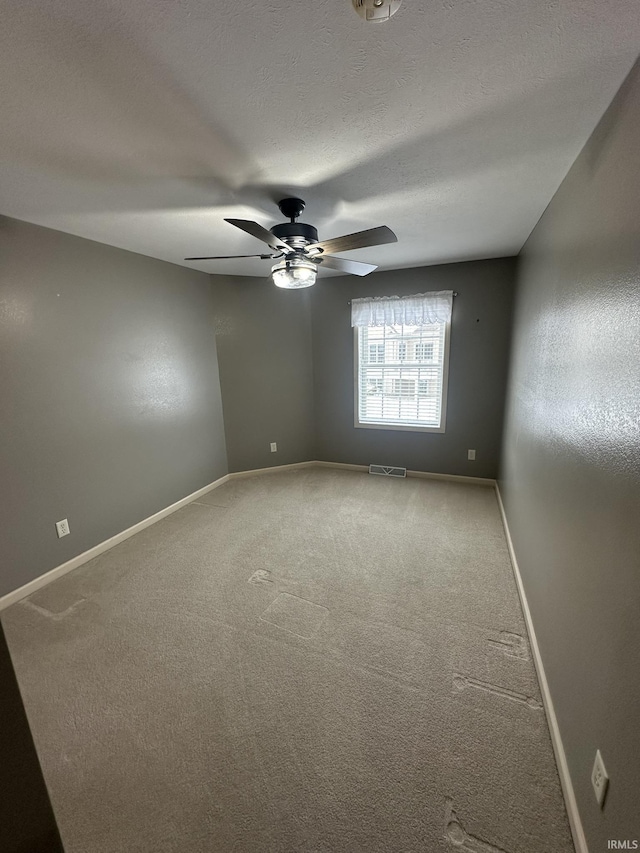 carpeted empty room with a ceiling fan, visible vents, baseboards, and a textured ceiling