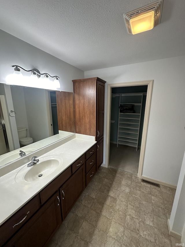 bathroom with a walk in closet, visible vents, toilet, vanity, and a textured ceiling