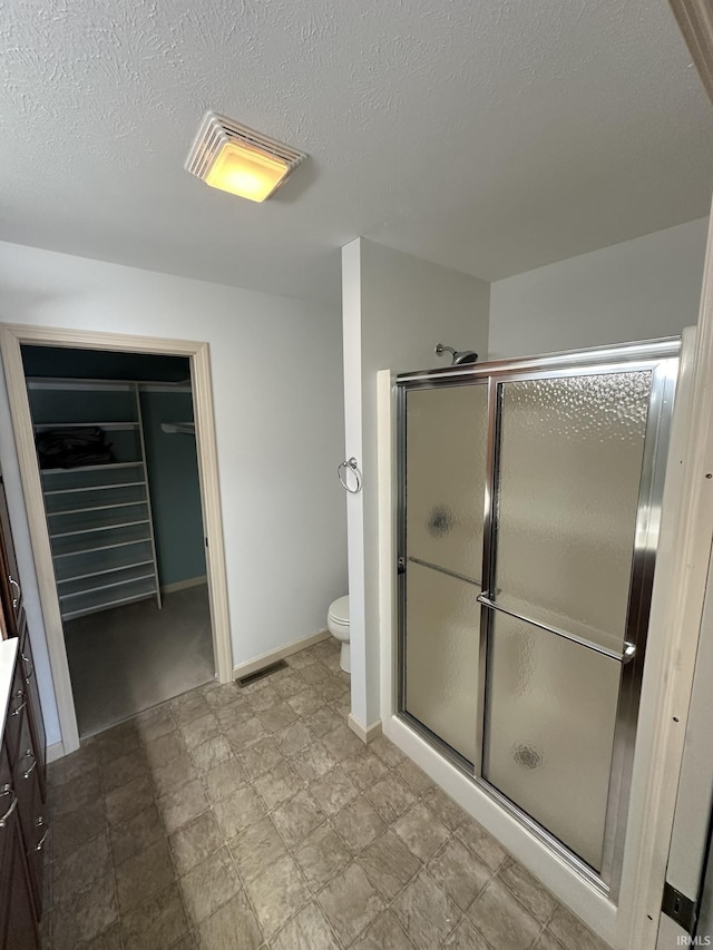 bathroom featuring visible vents, toilet, a shower stall, a textured ceiling, and baseboards