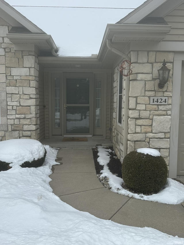 snow covered property entrance with stone siding