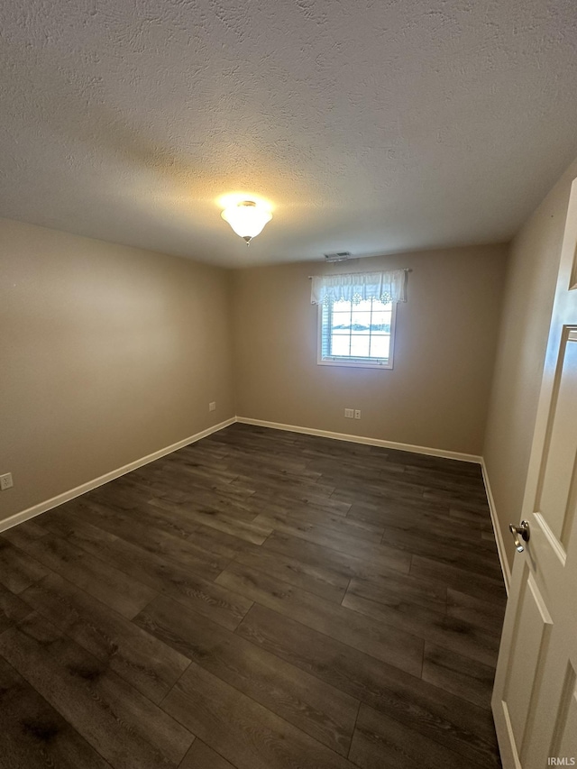 unfurnished room with visible vents, dark wood finished floors, a textured ceiling, and baseboards