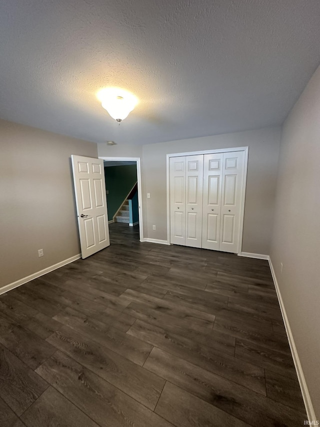 unfurnished bedroom featuring a closet, baseboards, dark wood finished floors, and a textured ceiling