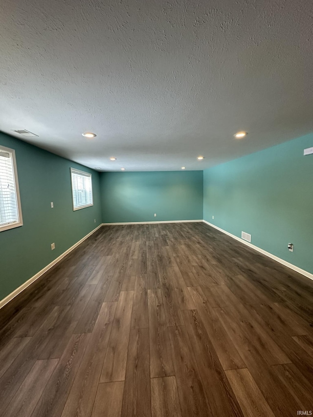 below grade area with a textured ceiling, dark wood-style flooring, visible vents, and baseboards