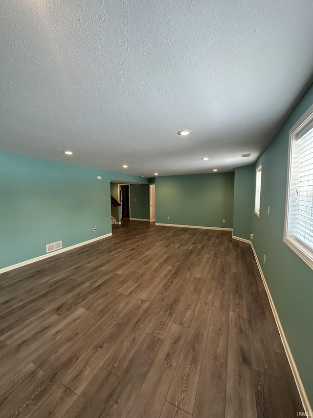 empty room featuring a textured ceiling, dark wood-style flooring, visible vents, and baseboards