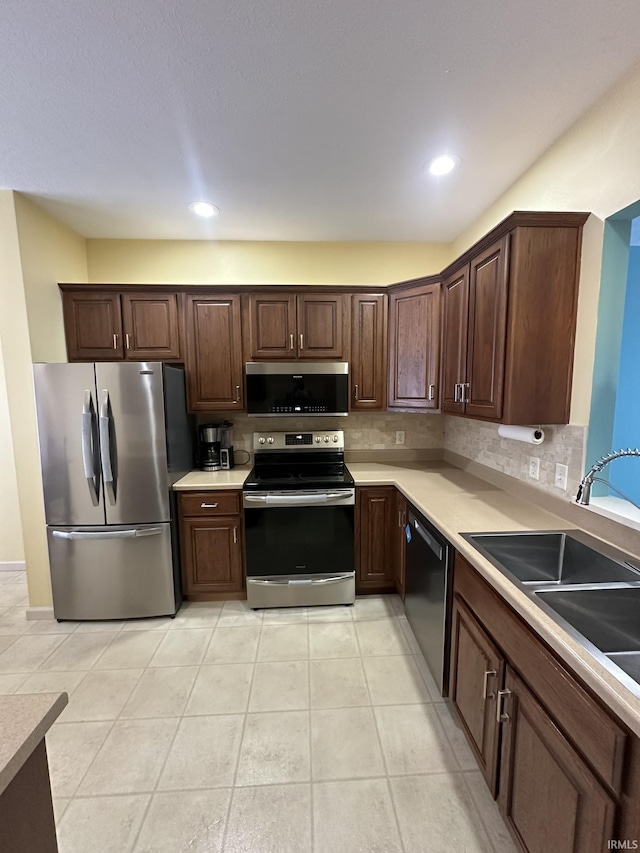 kitchen featuring light countertops, appliances with stainless steel finishes, a sink, and decorative backsplash