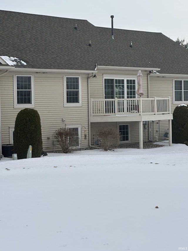 snow covered rear of property featuring roof with shingles