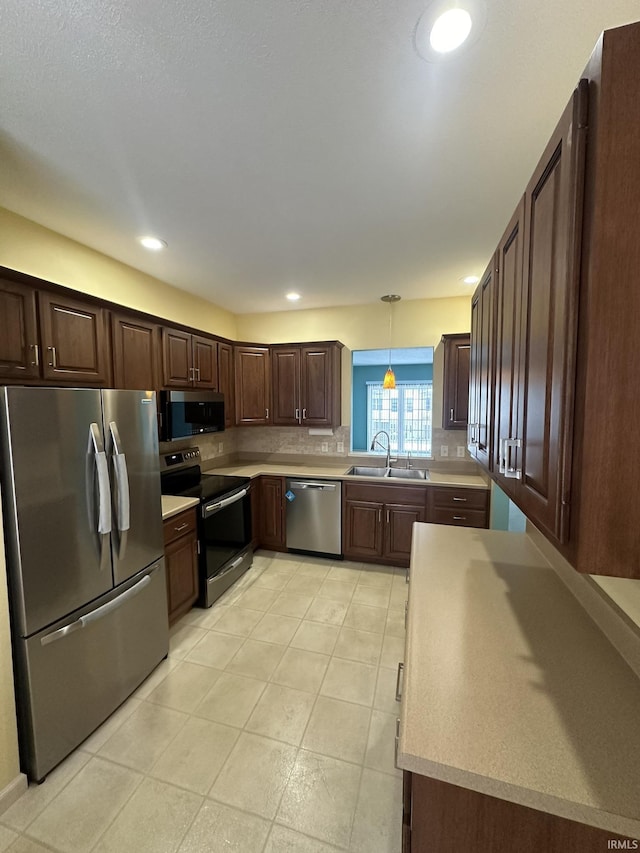 kitchen featuring dark brown cabinetry, a sink, light countertops, appliances with stainless steel finishes, and pendant lighting