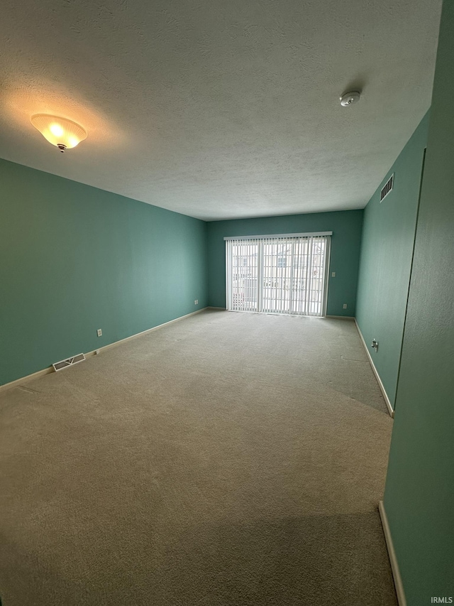 carpeted empty room with baseboards, visible vents, and a textured ceiling