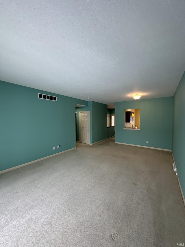 carpeted spare room with a textured ceiling, visible vents, and baseboards