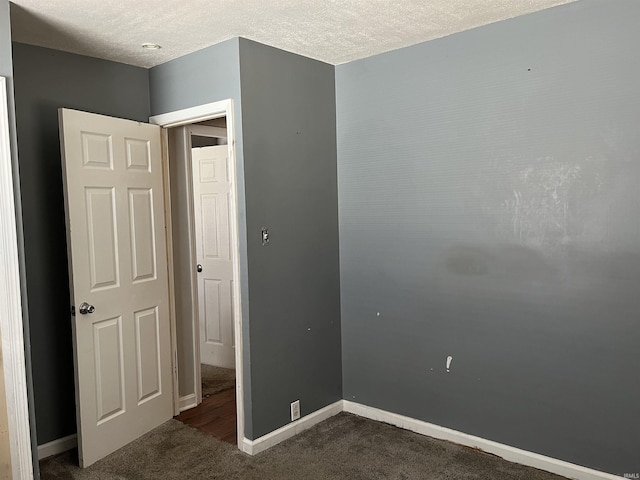 unfurnished bedroom with a textured ceiling, dark colored carpet, and baseboards