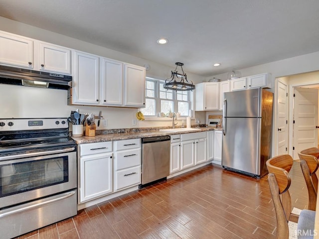 kitchen with stainless steel appliances, hanging light fixtures, white cabinetry, a sink, and under cabinet range hood