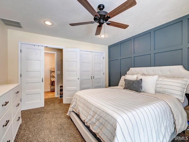 bedroom with visible vents, a ceiling fan, light colored carpet, a decorative wall, and a closet