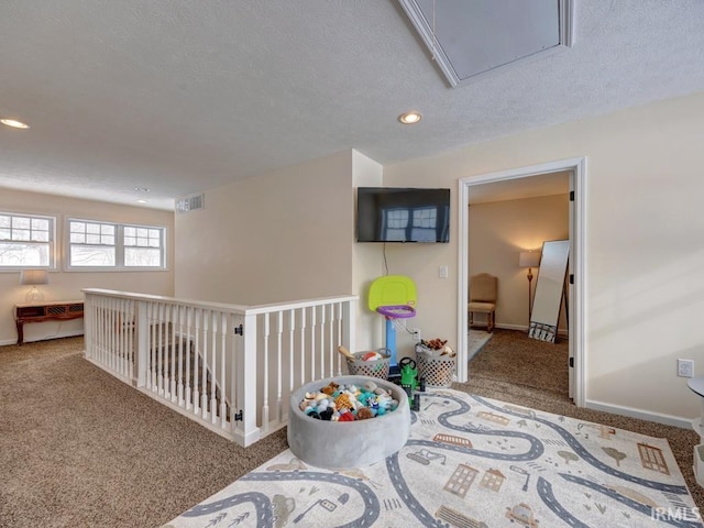 hallway with carpet, visible vents, attic access, a textured ceiling, and baseboards