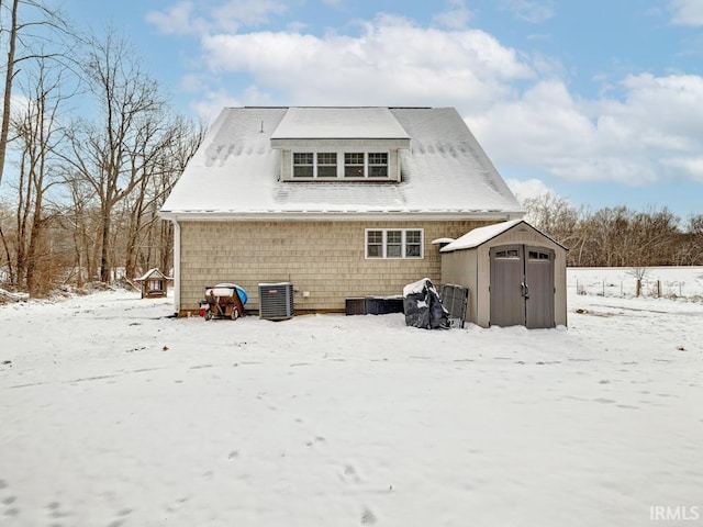 snow covered house featuring an outdoor structure, central AC unit, and a storage unit