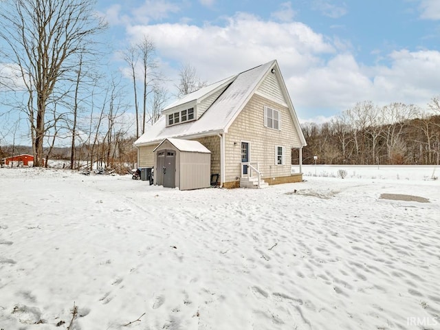 view of snow covered exterior featuring a garage, a storage unit, and an outdoor structure