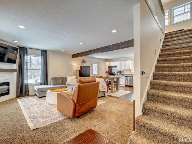 carpeted living area with a wealth of natural light, a glass covered fireplace, recessed lighting, and stairs