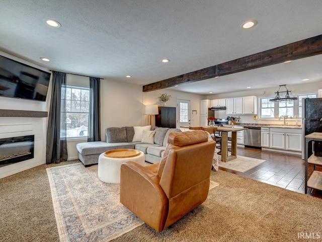 carpeted living area featuring a glass covered fireplace, beam ceiling, a healthy amount of sunlight, and recessed lighting