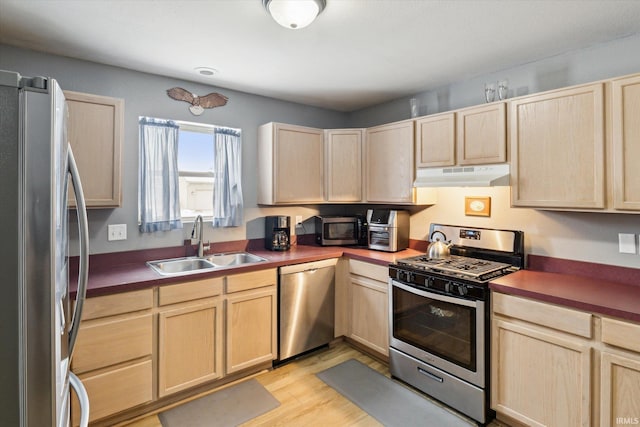 kitchen with stainless steel appliances, dark countertops, light brown cabinets, a sink, and under cabinet range hood