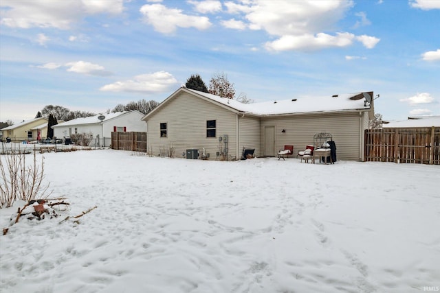 snow covered rear of property with central air condition unit and fence