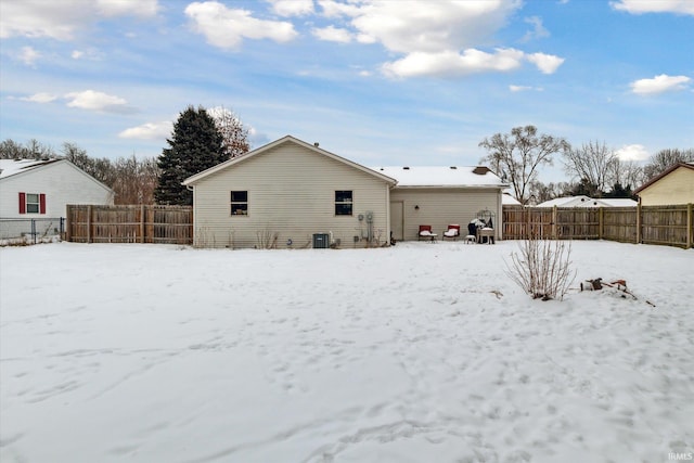 snow covered back of property featuring a garage, central AC unit, and a fenced backyard