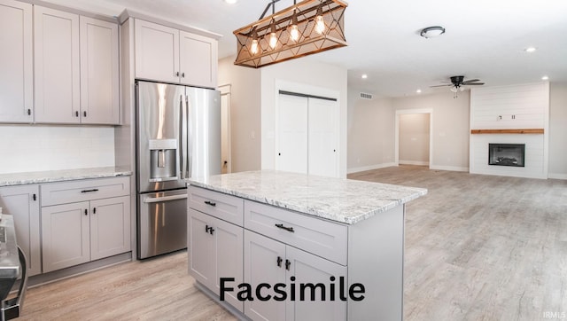 kitchen with a ceiling fan, stainless steel refrigerator with ice dispenser, gray cabinetry, a fireplace, and pendant lighting