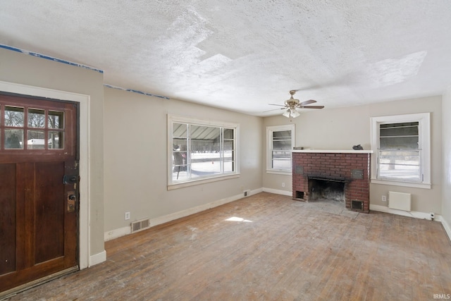 unfurnished living room featuring visible vents, a brick fireplace, a textured ceiling, wood finished floors, and baseboards