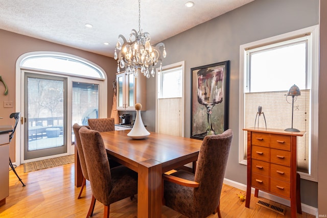 dining area with baseboards, visible vents, light wood-style flooring, a textured ceiling, and a notable chandelier