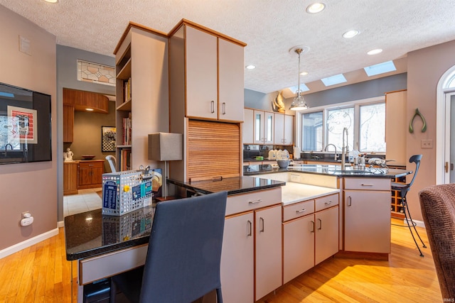 kitchen featuring light wood-style floors, decorative light fixtures, a peninsula, and a textured ceiling