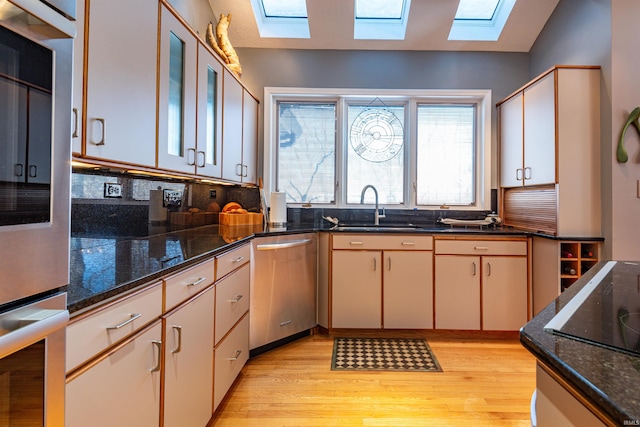 kitchen with dishwasher, light wood-style flooring, dark stone countertops, black electric cooktop, and a sink