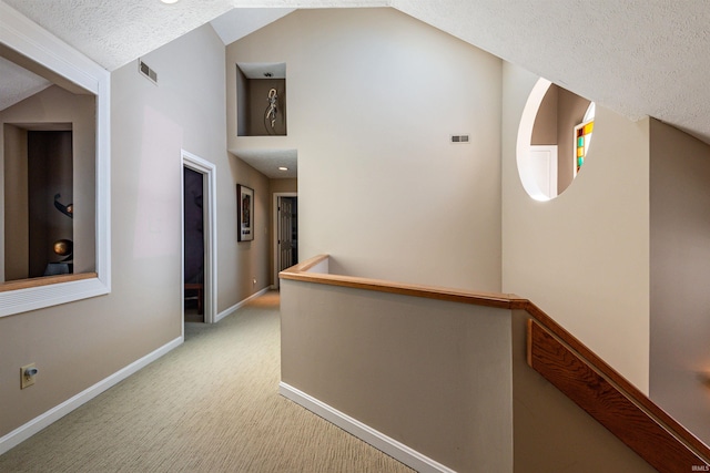 hallway with lofted ceiling, light colored carpet, a textured ceiling, and an upstairs landing