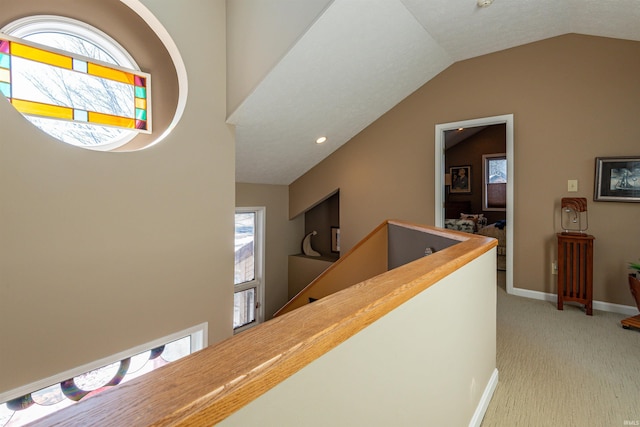 hall featuring lofted ceiling, an upstairs landing, baseboards, and light colored carpet